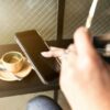 カフェでコーヒーのそばにスマートフォンを持つ手元