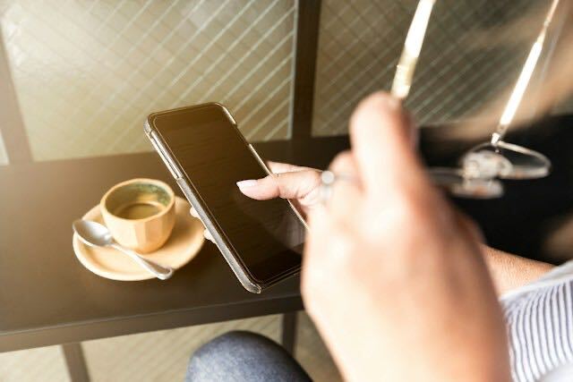 カフェでコーヒーのそばにスマートフォンを持つ手元