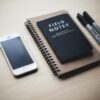 木のテーブルに置いたスマートフォン、ノート、ペン